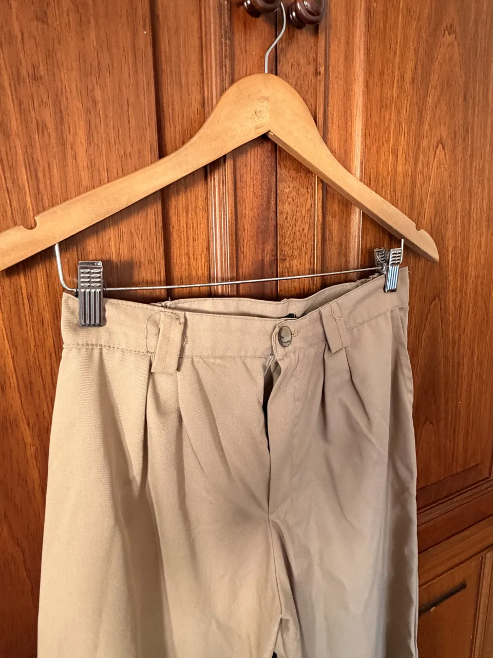 Pantalón de vestir color beige, con pinzas en la parte delantera y elástico en la cintura trasera. Cierre con botón y detalle de etiqueta con la marca "AMERICAN MIX" en la cintura.