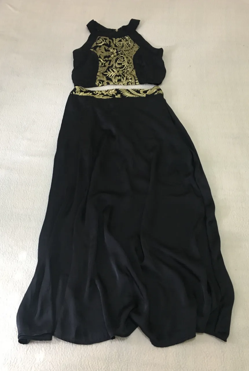 Conjunto de pollera larga y top negro con bordados dorados. El top es estilo halter con cierre en la espalda. La pollera es larga y fluida, con un detalle de bordado en la cintura.