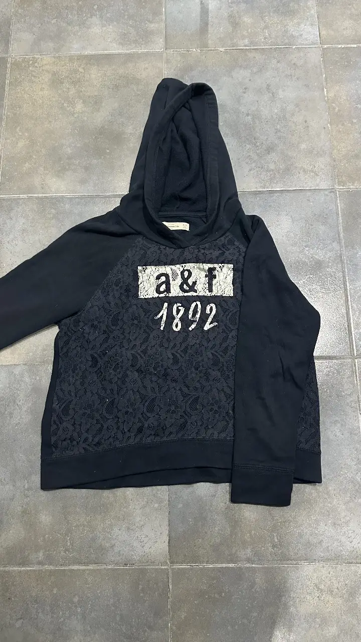 Buzo canguro azul marino de la marca Abercrombie & Fitch para niña, con detalle de encaje en el frente y logo de la marca. Ideal para un look casual y cómodo.