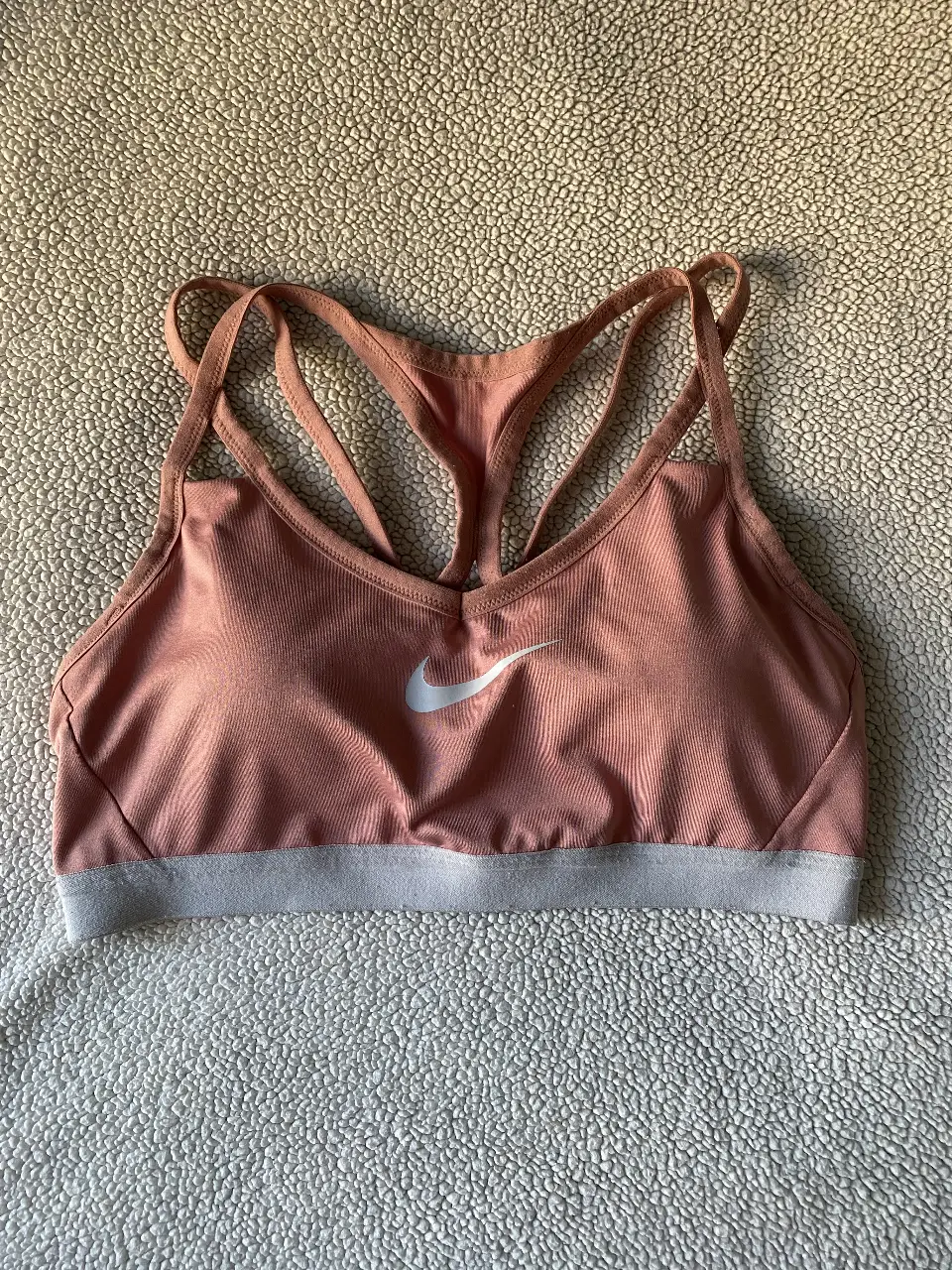 Top deportivo Nike color rosa con logo blanco. Ideal para entrenamientos y actividades de bajo impacto. Diseño con tirantes cruzados y espalda descubierta. 