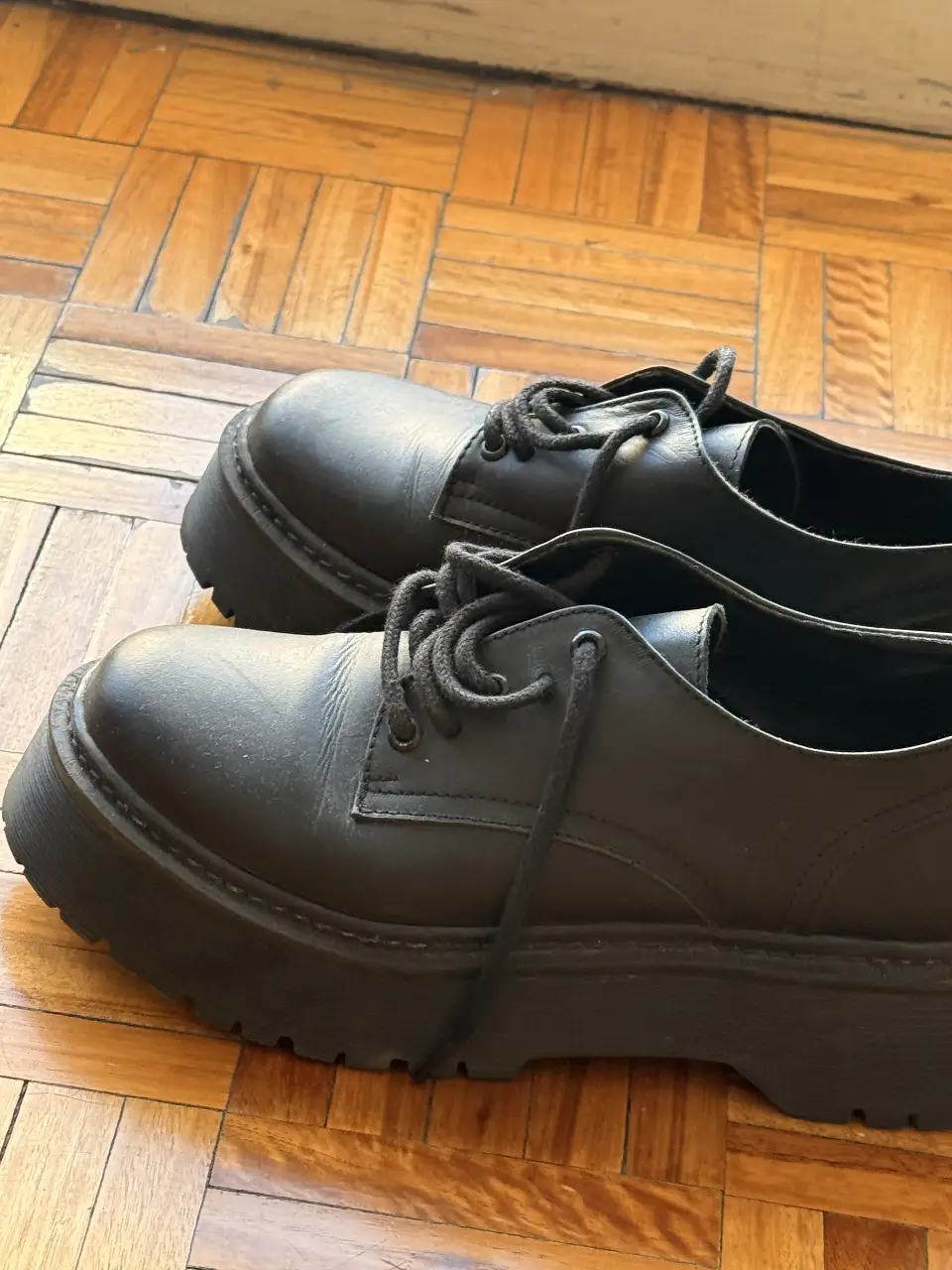 Zapatos de cuero negro con suela gruesa, ideales para un look moderno y urbano. Perfectos para combinar con diferentes estilos.