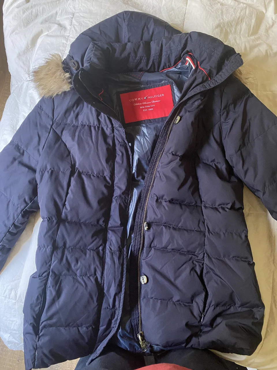 Campera Tommy Hilfiger de pluma para mujer, color azul marino con capucha desmontable y borde de piel sintética. Cuenta con cierre y botones, ideal para el invierno.