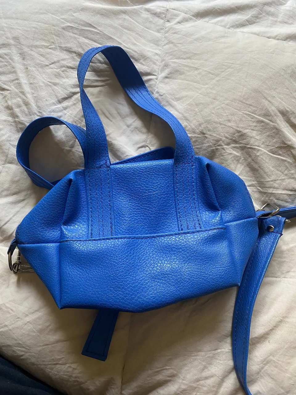 Cartera bandolera azul, con manijas cortas y correa larga ajustable. Diseño estructurado con textura similar al cuero, ideal para un look moderno y versátil.