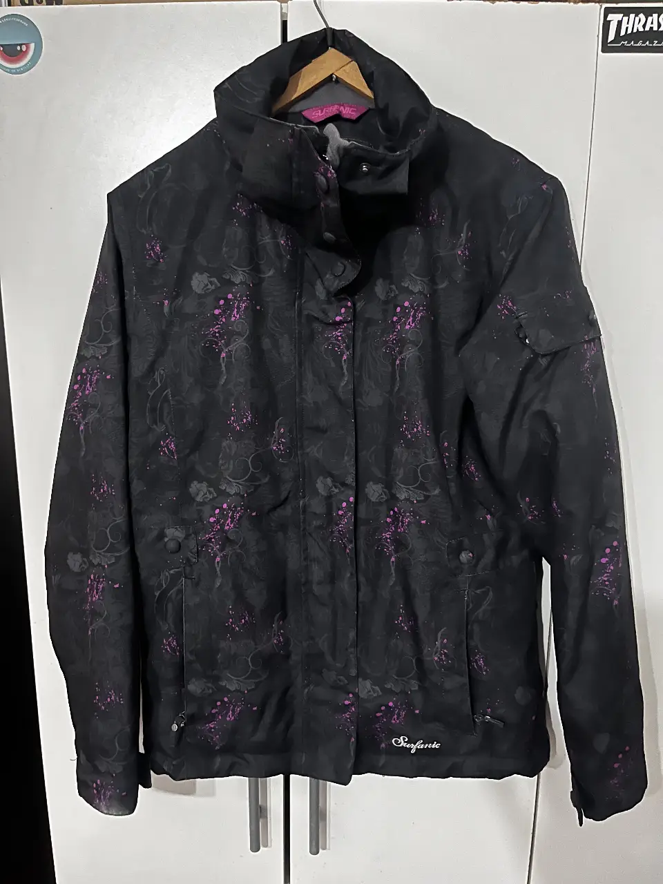 Campera de abrigo para mujer, de color negro con estampado floral en tonos violetas. Ideal para actividades al aire libre o uso diario en climas fríos. Posee cierre frontal, bolsillos y cuello alto.