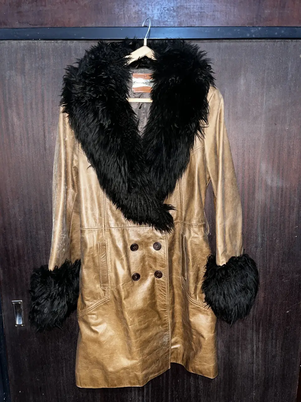 Tapado largo de cuero sintético color dorado con cuello y puños de piel sintética negra. Diseño vintage con botones y detalles de costura. Ideal para un look sofisticado y abrigado.