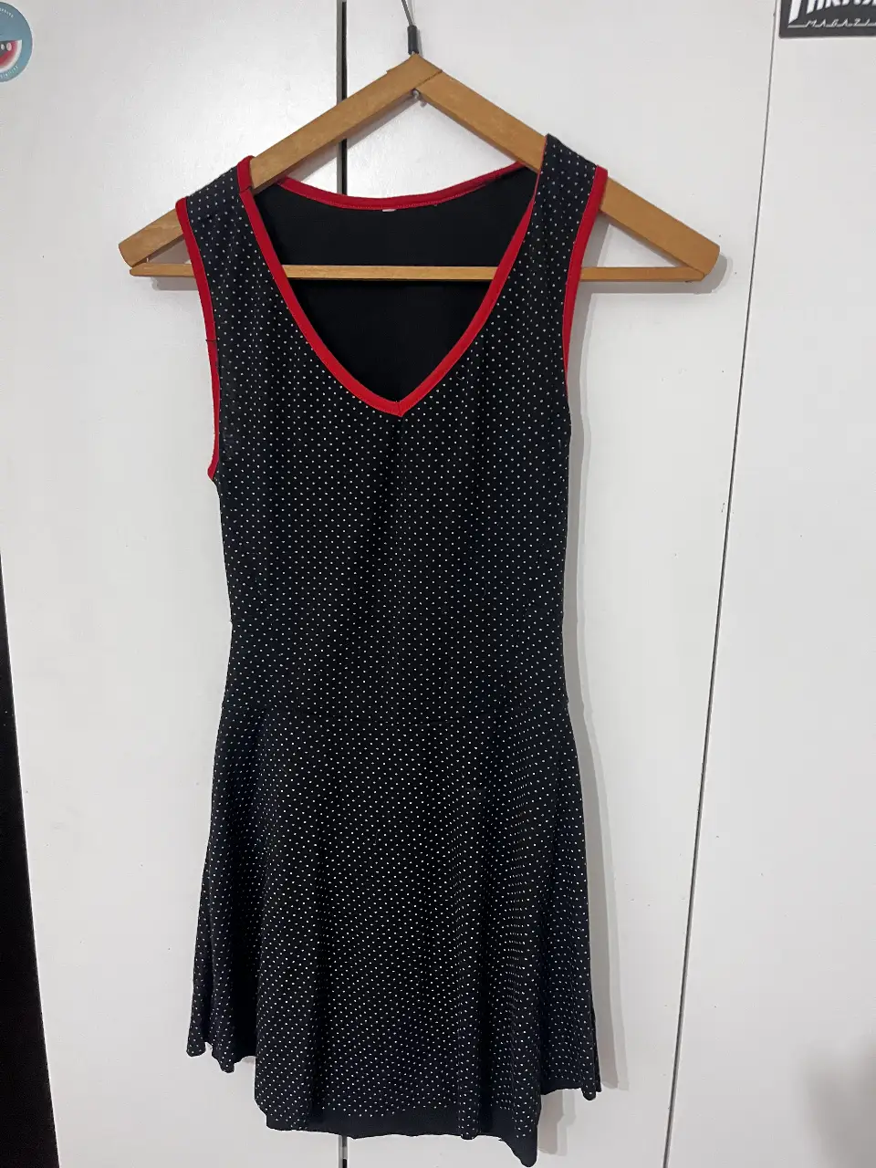 Vestido mini negro con lunares blancos y detalles en rojo. Diseño con escote en V y espalda descubierta con borde rojo. Ideal para una salida casual o una fiesta.
