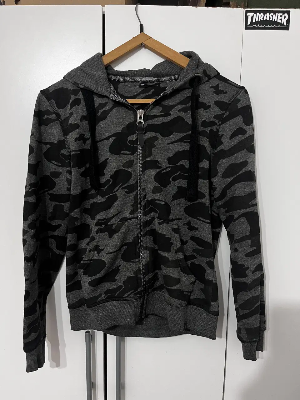 Buzo con cierre y capucha para hombre, con estampado camuflado en tonos grises y negros. Ideal para un look casual y urbano.