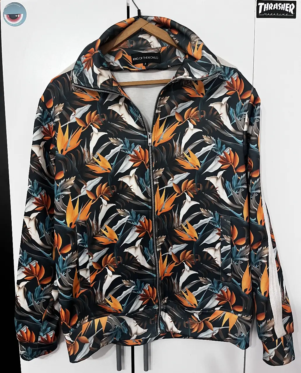 Buzo con cierre para hombre, con estampado floral en tonos naranja, blanco y negro. Ideal para un look casual y moderno.