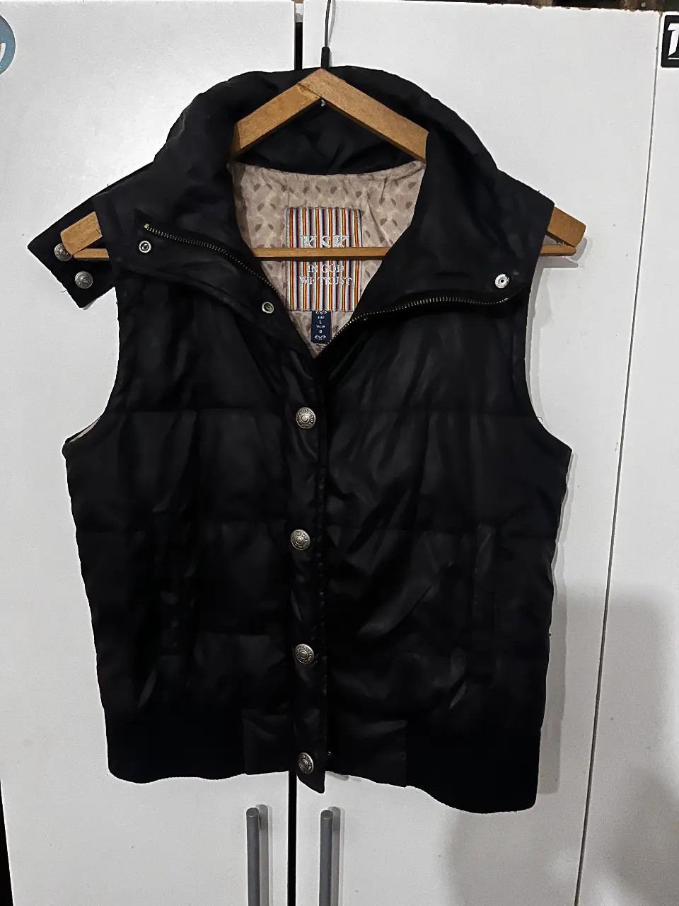 Chaleco negro acolchado para mujer, con cuello alto y botones plateados. Ideal para el invierno, con un diseño clásico y versátil.
