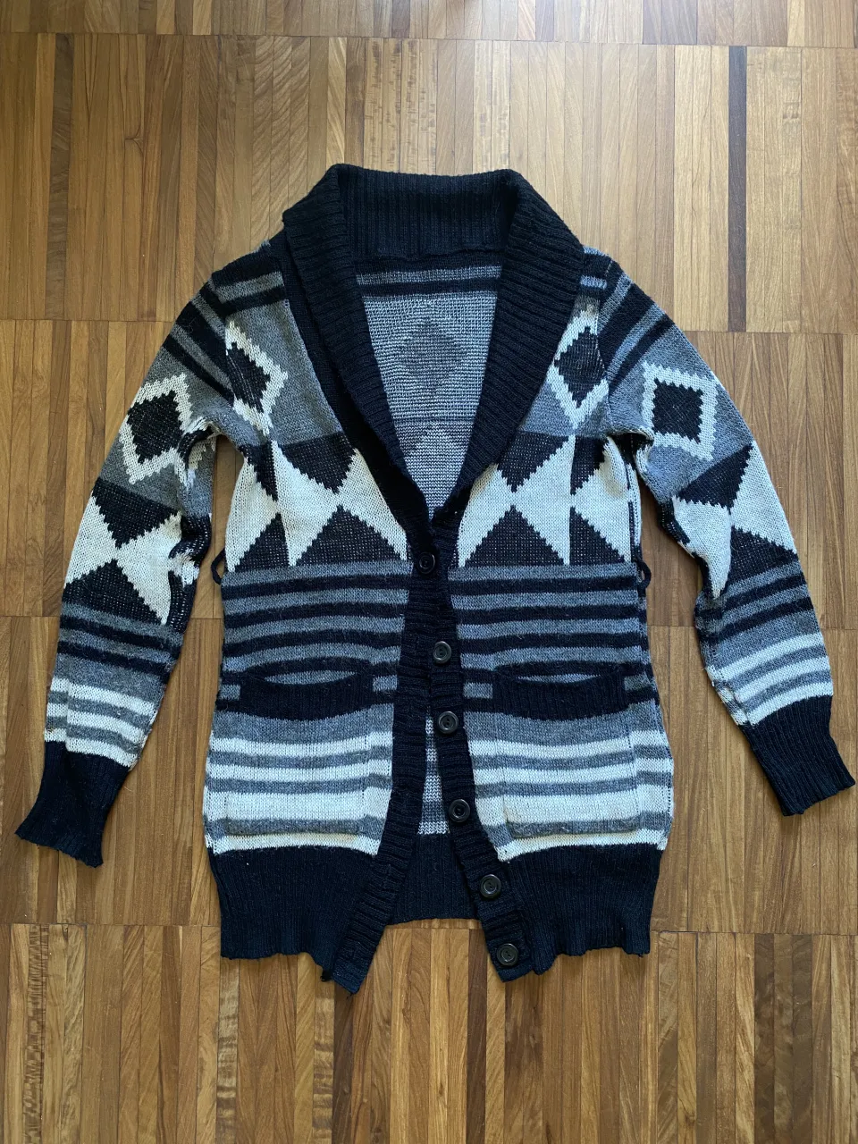 Cardigan tejido con diseño geométrico en blanco, negro y gris. Posee cuello solapa, botones al frente y bolsillos laterales. Ideal para un look casual, cómodo y abrigado. Talle S/M