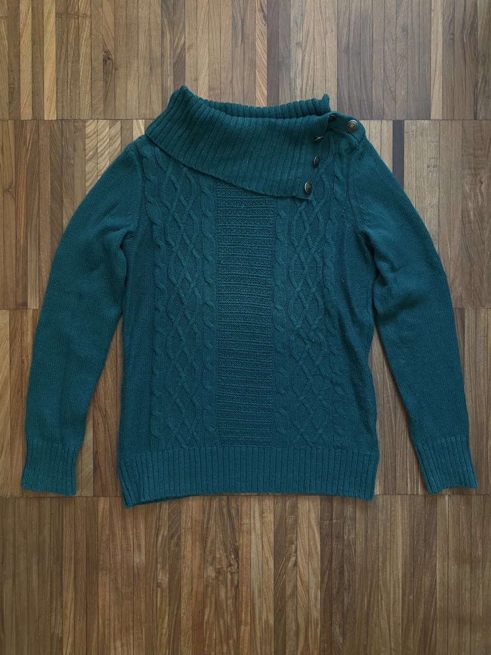 Sweater de lana verde oscuro con cuello polera asimétrico y detalles de trenzas. Tiene botones en el cuello y es ideal para un look canchero y abrigado. 