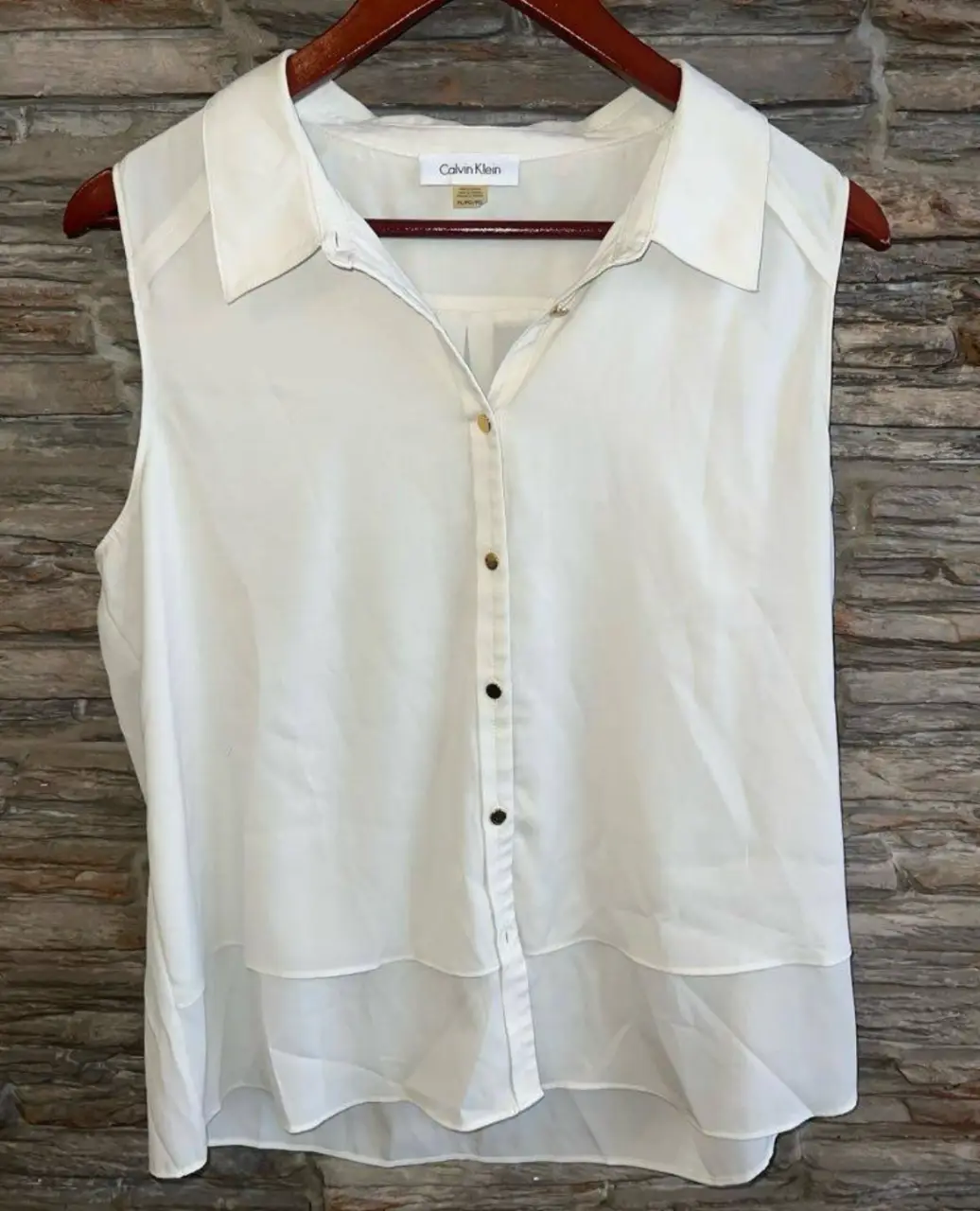 Blusa sin mangas de Calvin Klein, blanca, con botones dorados y detalle de doble capa en la parte inferior. Ideal para un look elegante y fresco.