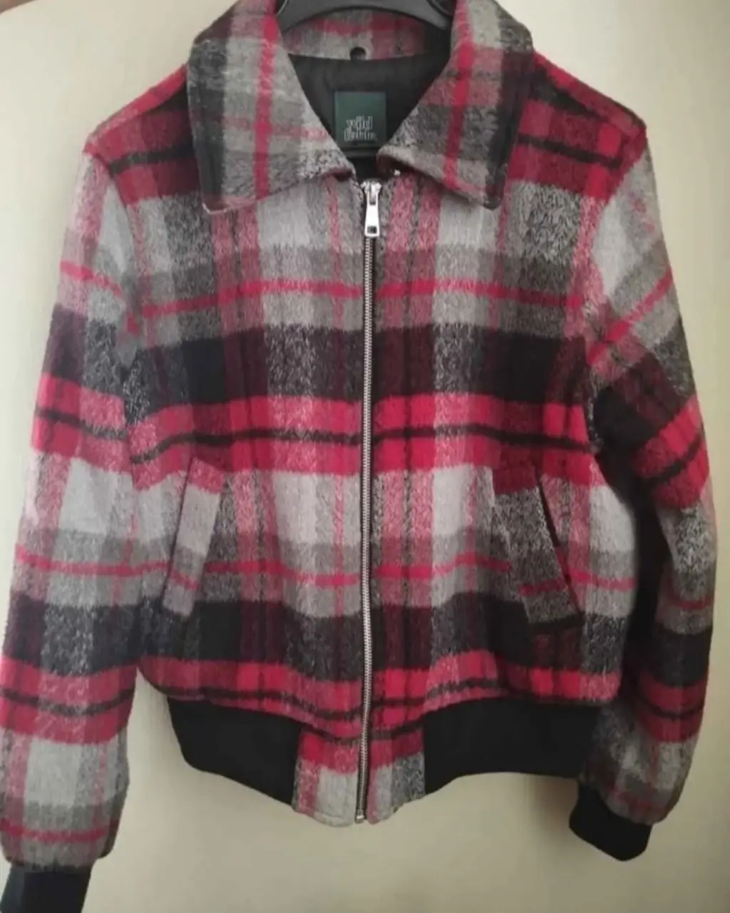 Campera bomber a cuadros en tonos rojos, grises y negros, con cierre frontal y forro interior negro. Ideal para un look casual y abrigado.