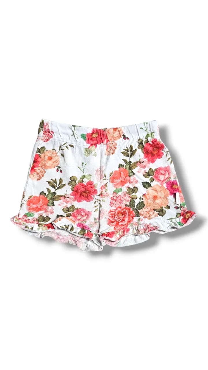 Shorts blancos con estampa floral de rosas en tonos rojos, rosas y naranjas. Tienen cintura elastizada y volados en los bordes inferiores. Ideales para un look fresco y femenino. Es 100% algodón. 
