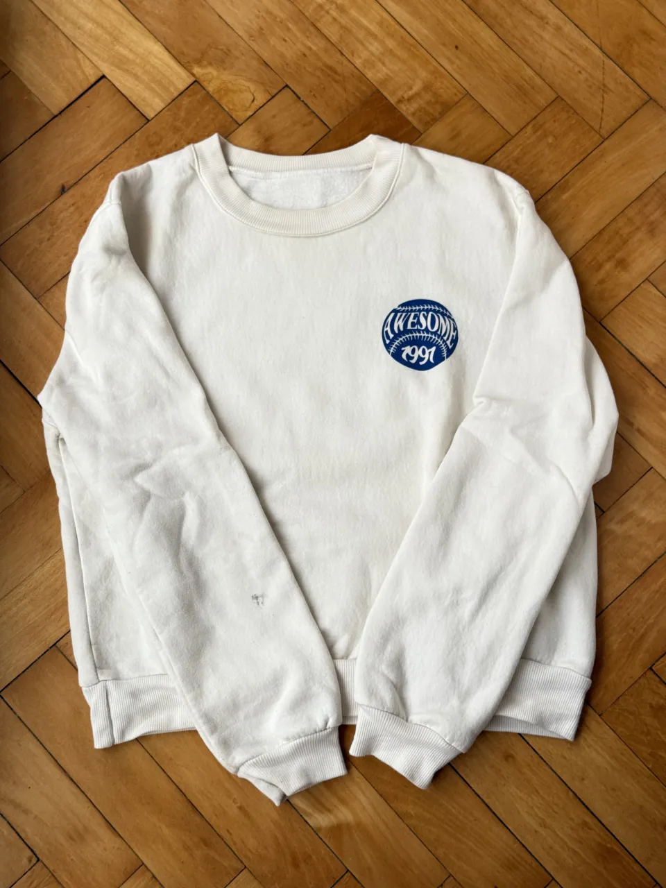 Buzo blanco con estampa "Amazing Teamwork" en la espalda y "Awesome 1991" en el frente. Ideal para un look casual y relajado.
Pequeña mancha negra en una marga 