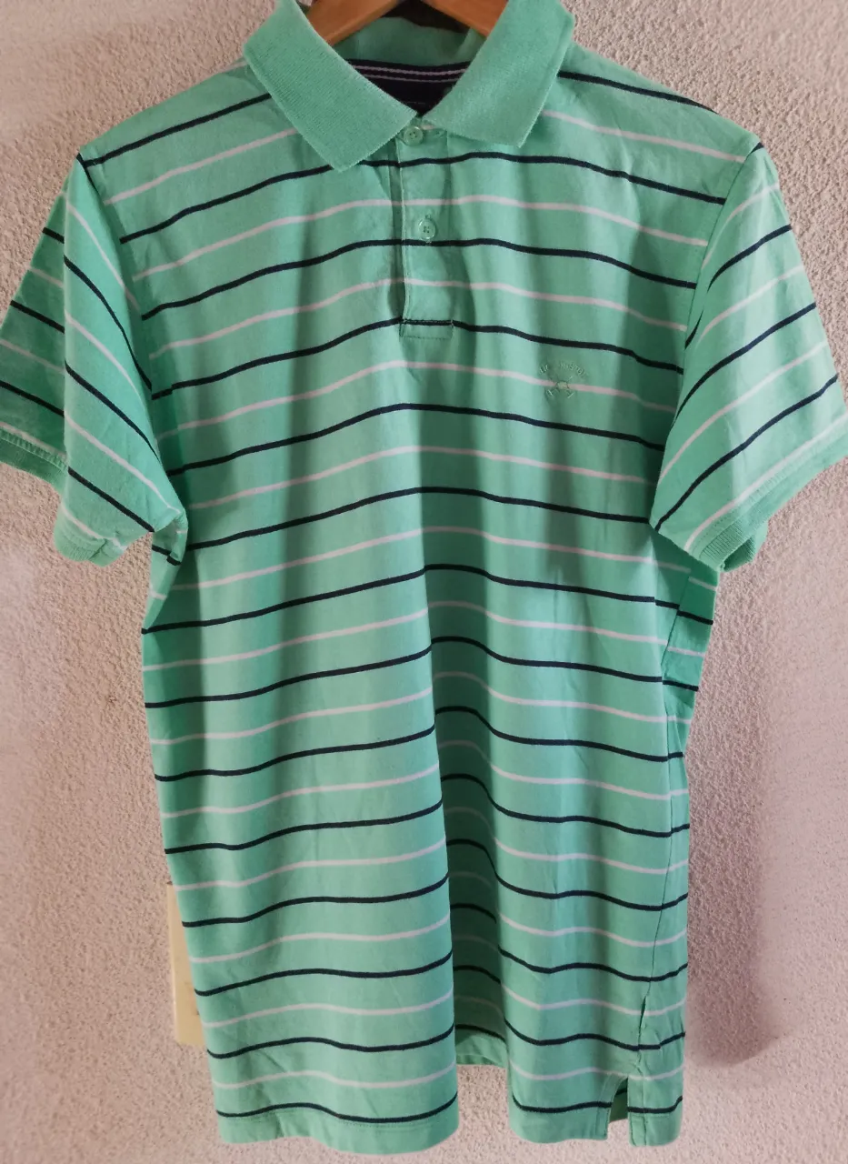 Remera a rayas celestes, blancas y azul marino. Posee cuello tipo polo con dos botones y manga corta.