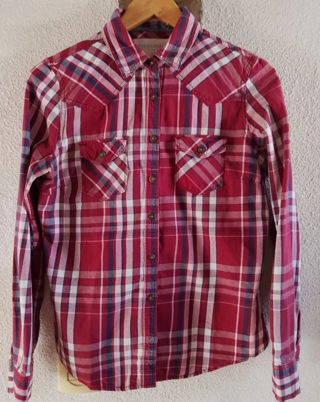Camisa a cuadros de manga larga con botones al frente y dos bolsillos en el pecho. La camisa tiene un estampado a cuadros en tonos rojos, blancos y azules.