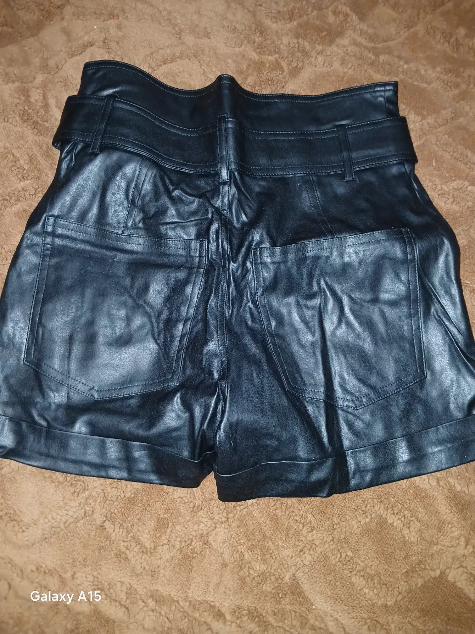 Short de cuero sintético negro, tiro alto, con cinturón y bolsillos. Ideal para un look moderno y audaz.