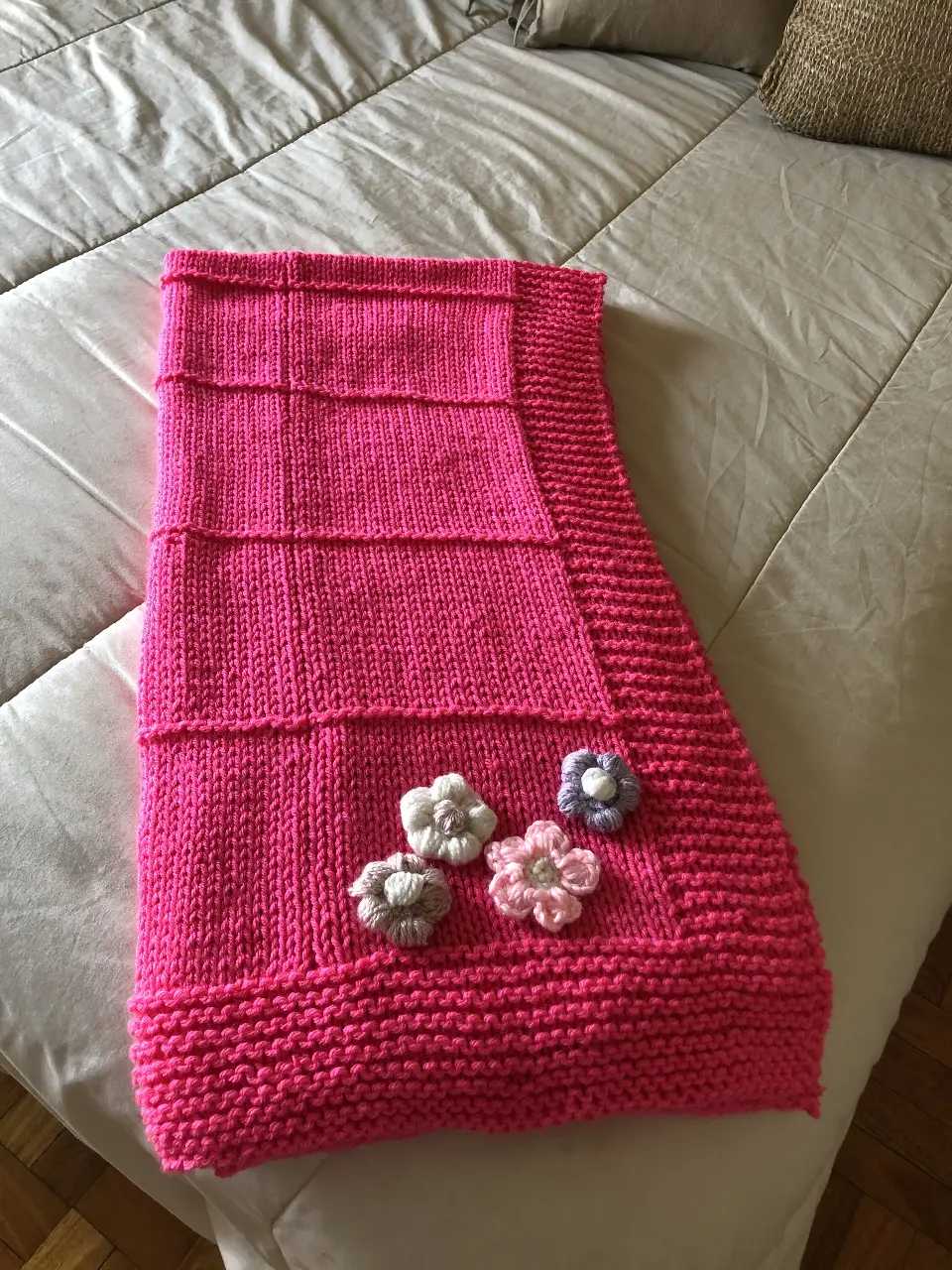 Hermosa manta tejida a mano en color rosa, adornada con flores aplicadas. Ideal para abrigar y decorar cualquier espacio.