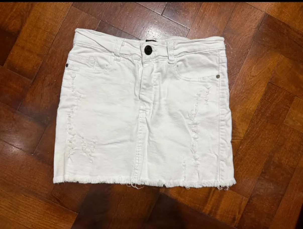 Pollera de jean blanca, tiro alto, con roturas y detalles deshilachados en los bordes. Un básico canchero para cualquier look.