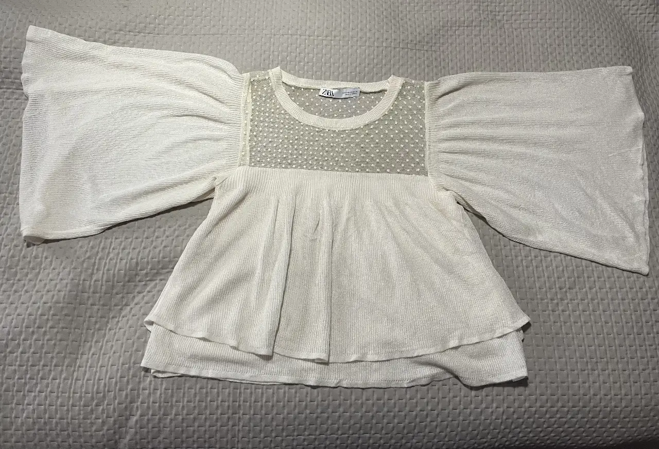 Blusa blanca de tejido texturado con mangas amplias y detalle de encaje en el pecho. Ideal para un look elegante y moderno.