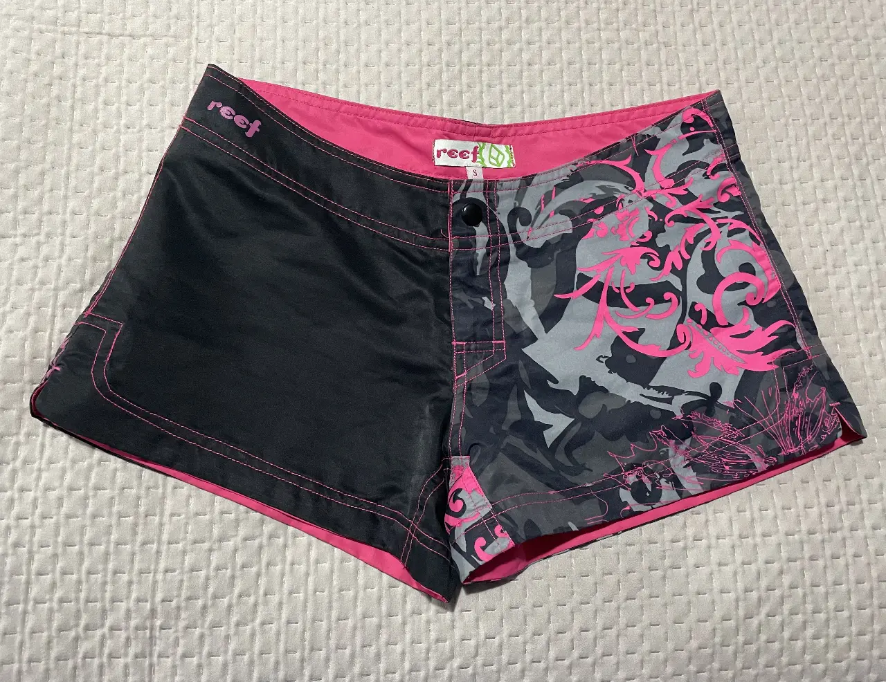 Short deportivo Reef para mujer, con diseño bicolor en negro y estampado en tonos grises y rosas. Ideal para actividades acuáticas o uso casual.