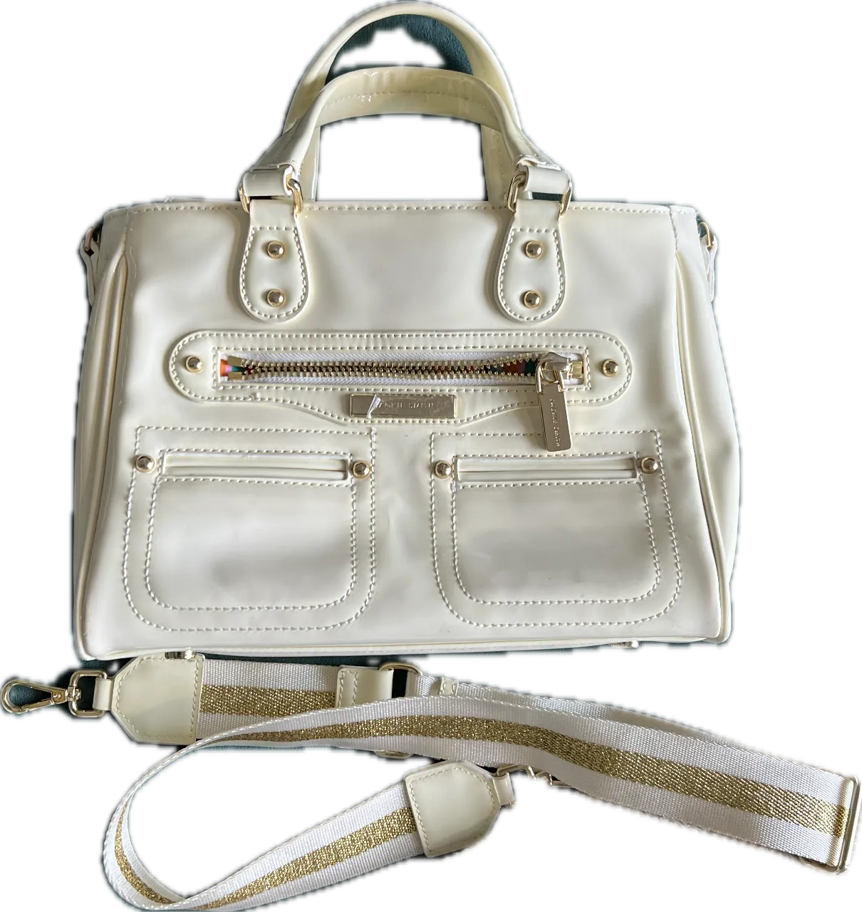 Cartera color crema Jackie Smith Bellini con detalles dorados y correa ajustable. Diseño elegante con dos bolsillos frontales y cierre. Ideal para un look sofisticado.