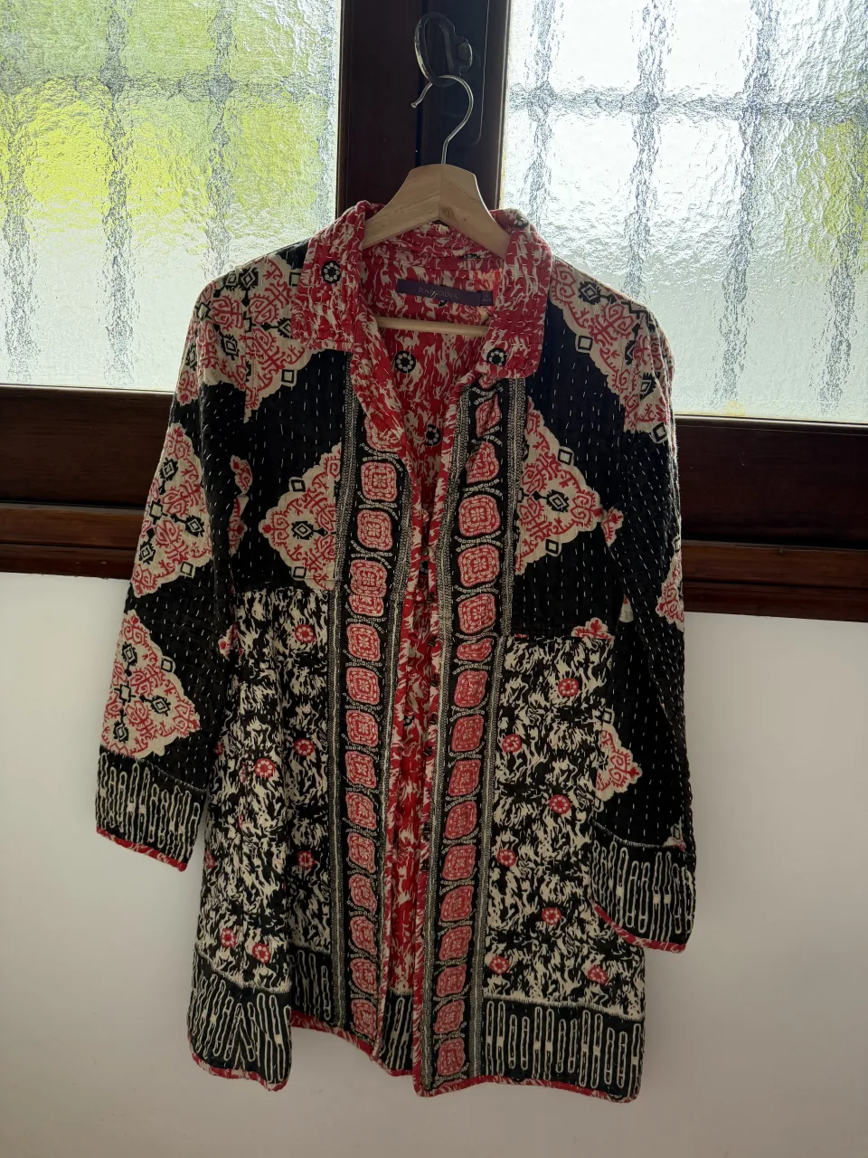 Campera estampada con motivos florales y geométricos en tonos rojo, negro y blanco. Posee cuello camisero y mangas largas.