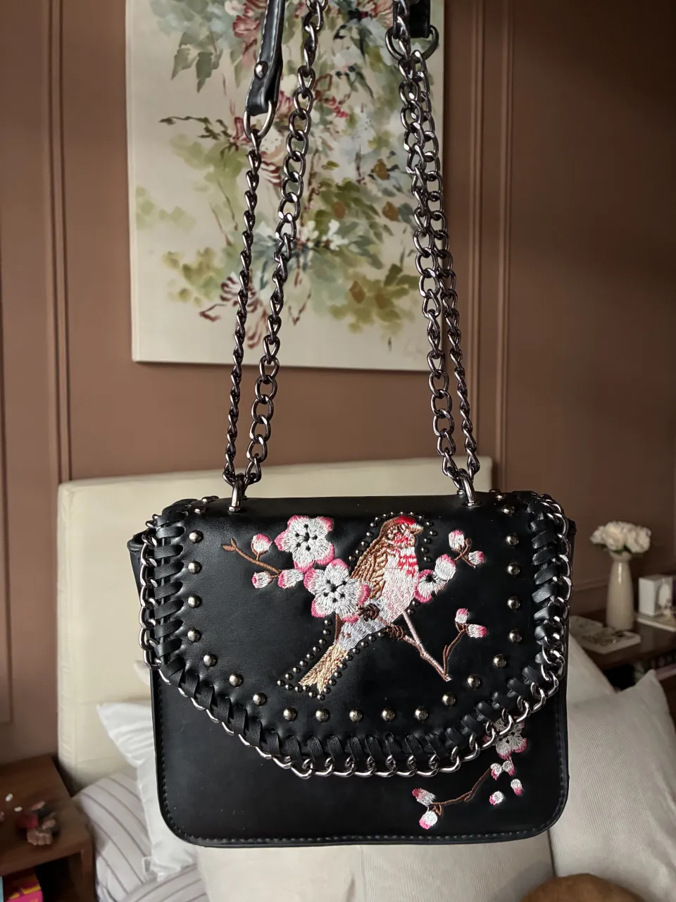 Cartera negra con bordado de pájaro y flores de cerezo. Posee detalles de tachas plateadas y cadena metálica como correa.