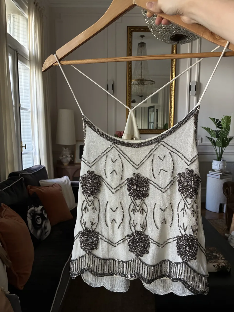 Top blanco con tiras finas y detalles de canutillos plateados y negros. Presenta un diseño geométrico y floral bordado con canutillos en toda la prenda. El borde inferior es ondulado y también está decorado con canutillos.