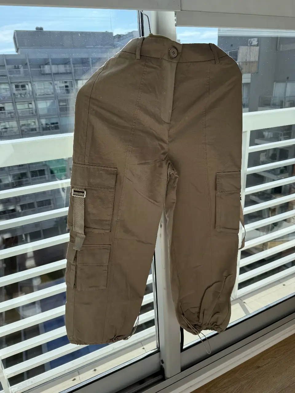 Pantalón cargo color khaki de mujer, tiro medio, con bolsillos laterales y detalles de ajuste en los tobillos. Ideal para un look casual y moderno.