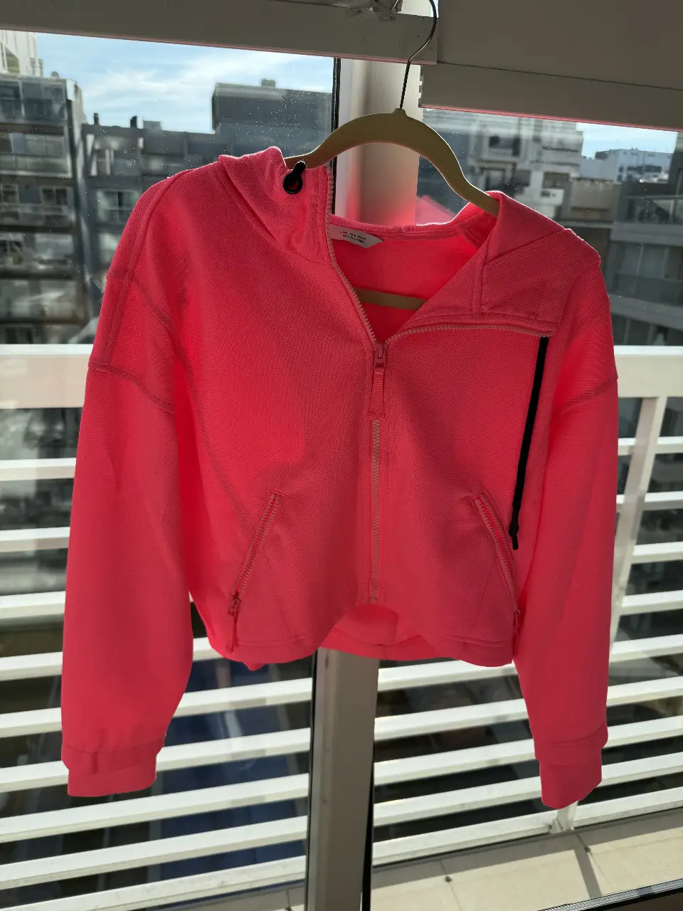 Buzo con cierre de color rosa chicle, con capucha y bolsillos. Ideal para un look deportivo y canchero.