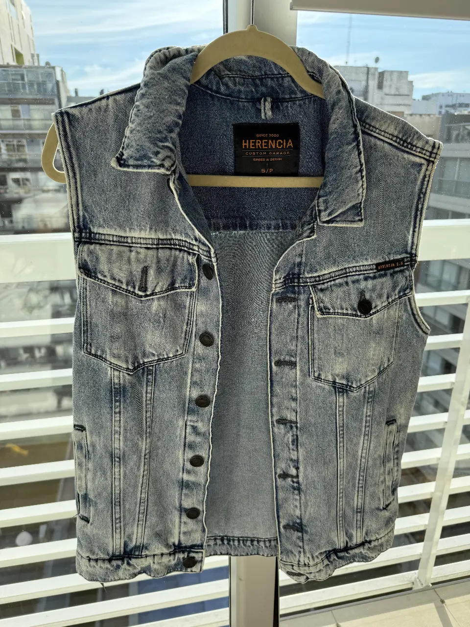 Chaleco de jean azul claro, sin mangas, con botones y bolsillos. Ideal para un look casual y canchero. Marca Herencia, talle S/P.