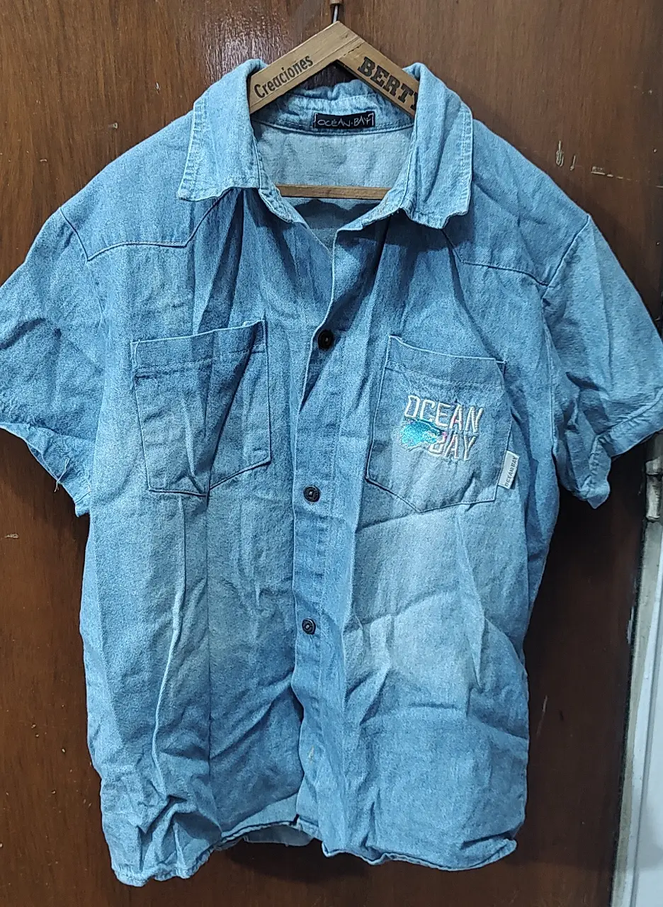Camisa de jean celeste con bordado "OCEAN BAY" en el bolsillo. Talle 14. Con botones de metal. Ideal para un look casual y relajados.