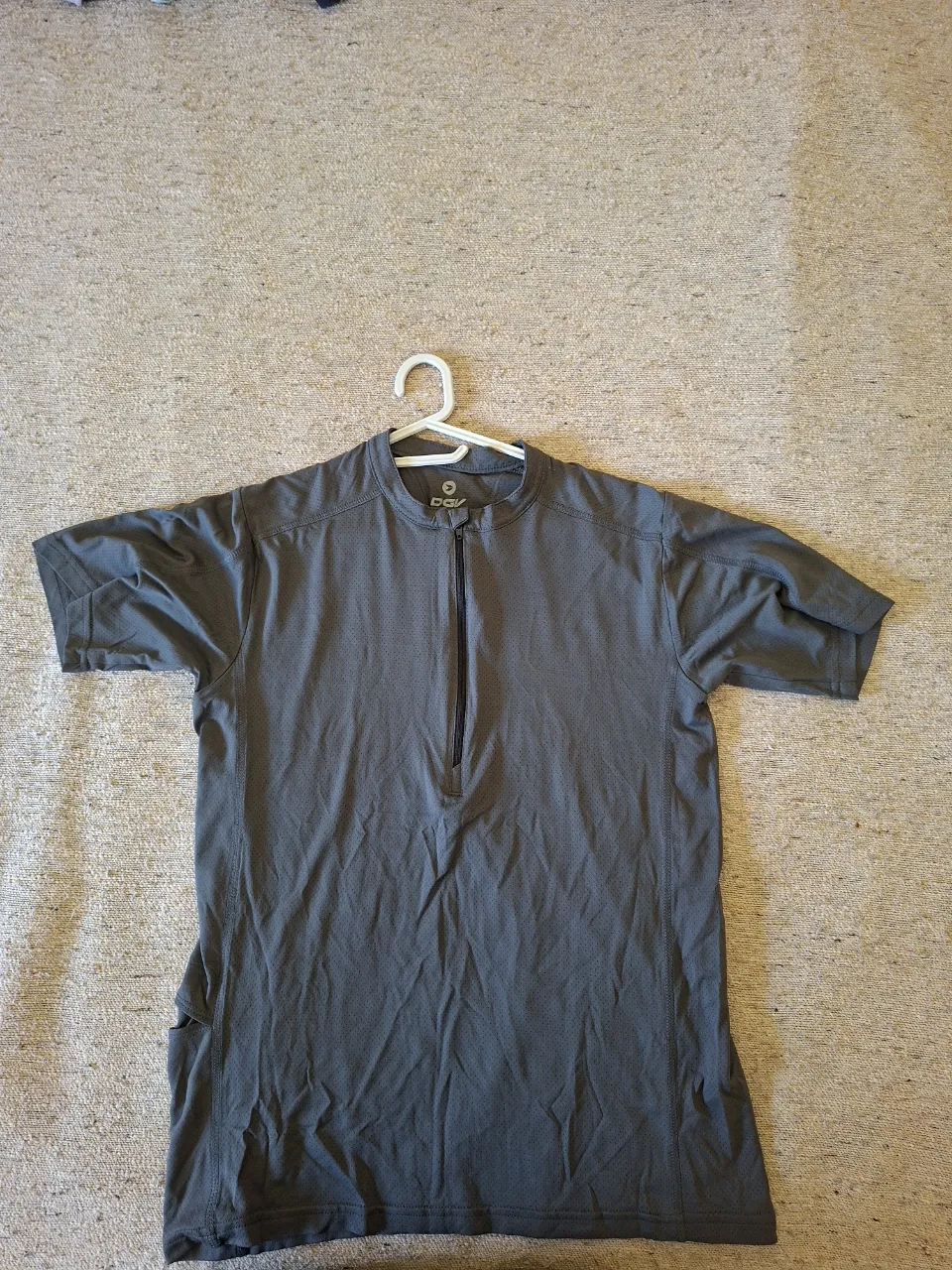 Remera deportiva de hombre, color gris oscuro, con cierre frontal y manga corta. Ideal para actividades físicas.