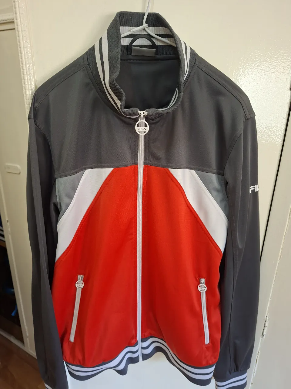 Campera deportiva Fila para hombre, con cierre frontal, detalles en blanco y rojo. Ideal para actividades deportivas o uso casual.