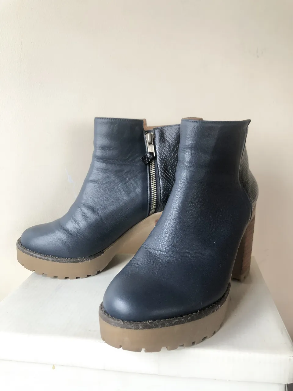 Botines de cuero azul marino con plataforma y taco de madera. Detalles en símil piel de serpiente en la parte trasera. Cierre lateral con cremallera.