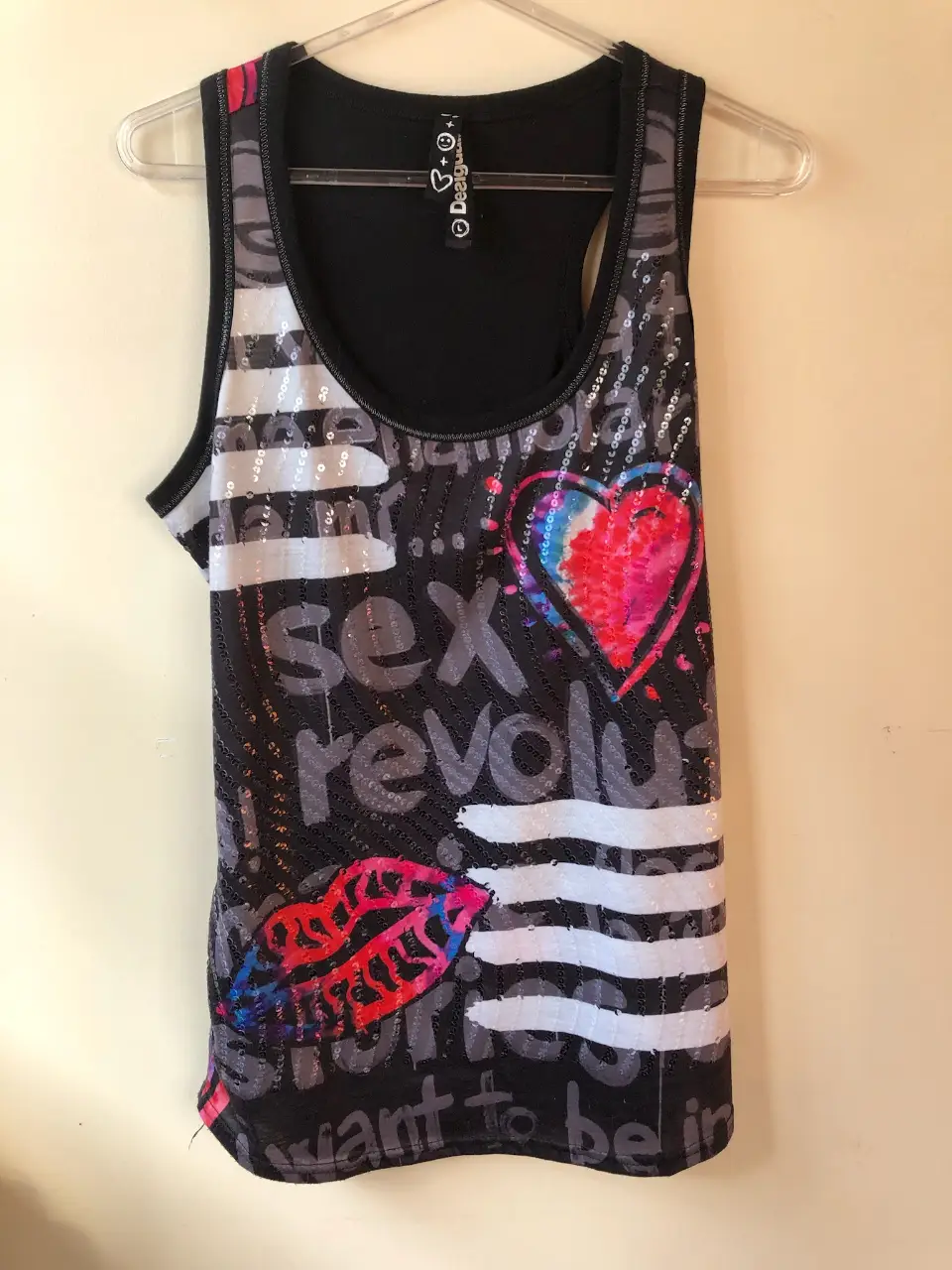 Musculosa Desigual con diseño vibrante. Estampado con palabras y frases en gris, detalles de lentejuelas. Ideal para un look moderno y llamativo.