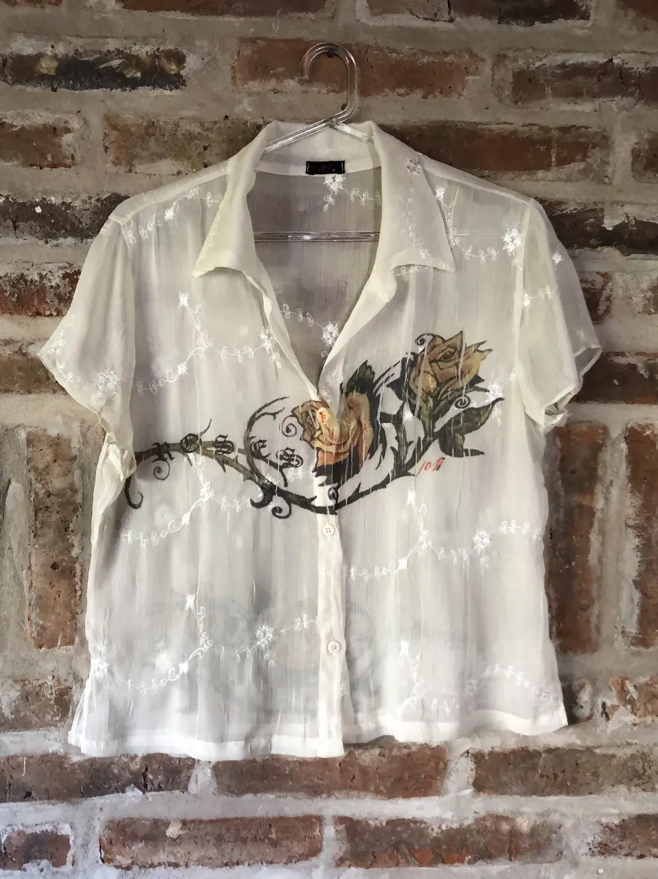 Blusa de manga corta blanca transparentara, con estampado floral en tonos amarillos y detalles de encaje. Ideal para un look vintage,  suave y fresco.