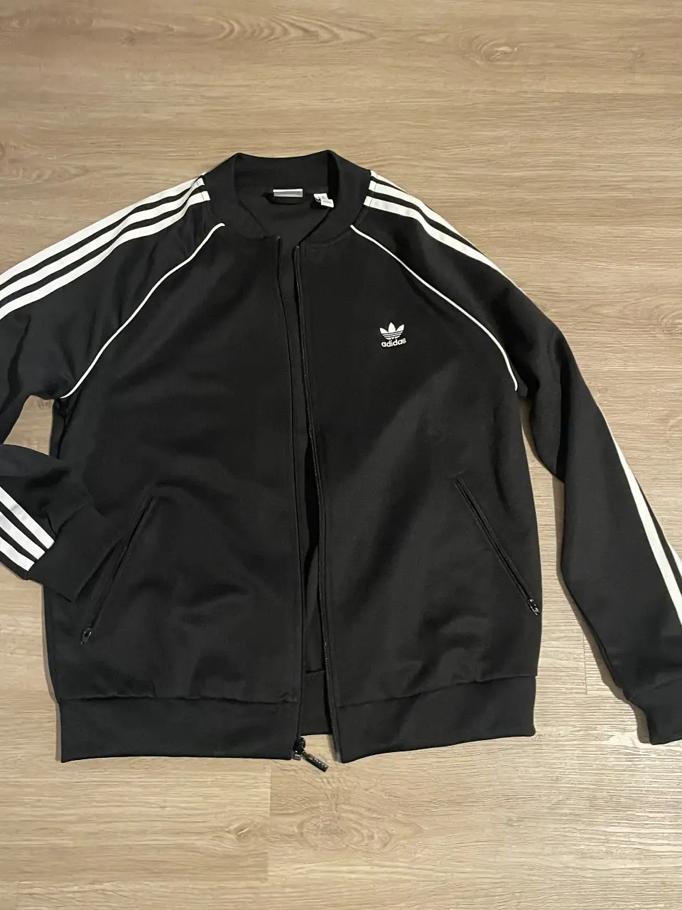 Campera Adidas negra con las tres tiras blancas en las mangas y el logo de la marca en el pecho. Ideal para un look deportivo y casual.
