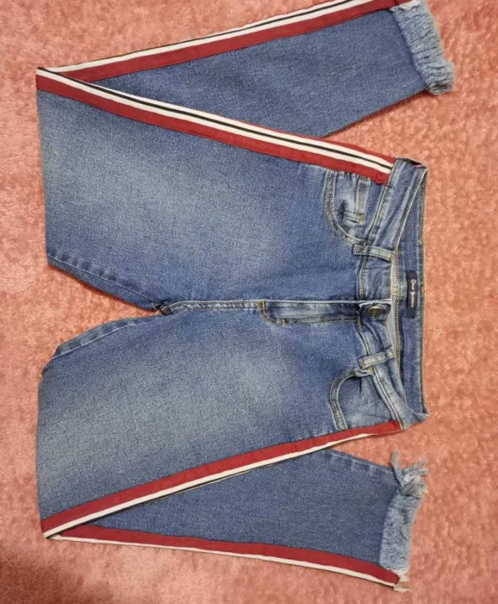 Jean marca Como Quieres, talle 26/36, tiro alto, elastizado, con franjas laterales rojas y blancas. Poseen roturas y terminación desflecada en los tobillos. Medidas aprox en plano: cinturq 36 cm, tiro delantero 25 cm, tiro trasero 34 cm, largo 86 cm.