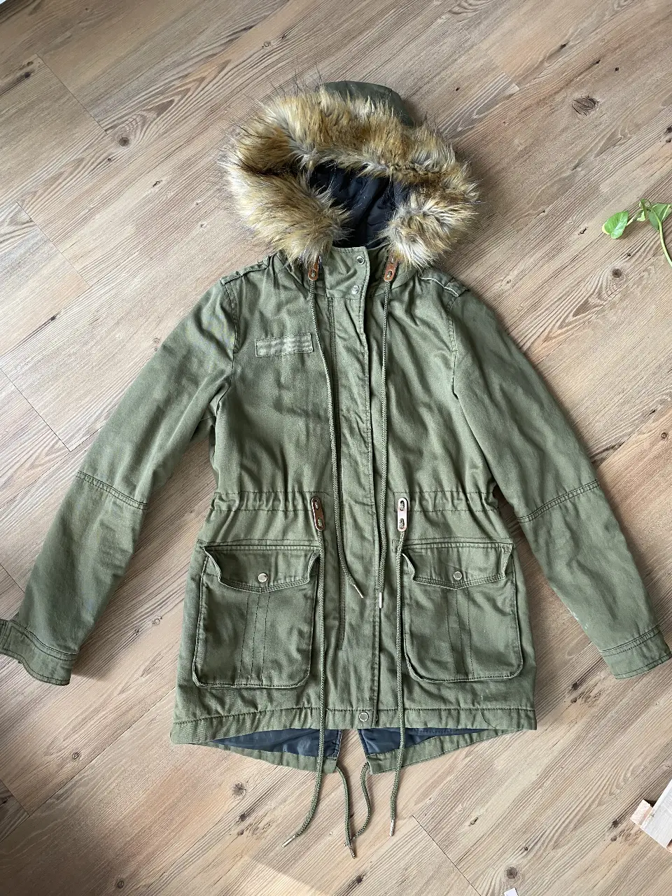 Campera parka verde militar con capucha de piel sintética. Posee bolsillos amplios y cordones ajustables en la cintura y en el bajo. Ideal para el invierno.