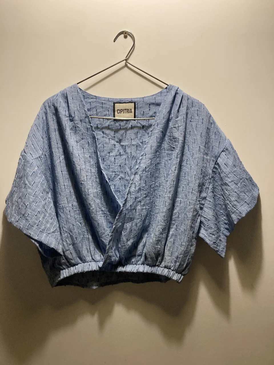 Blusa crop de lino azul con diseño cruzado y mangas cortas. Ideal para un look fresco y moderno. Confeccionada en tela liviana con textura rayada en tono azul. Con elástico a la cintura. Talle M/L. 