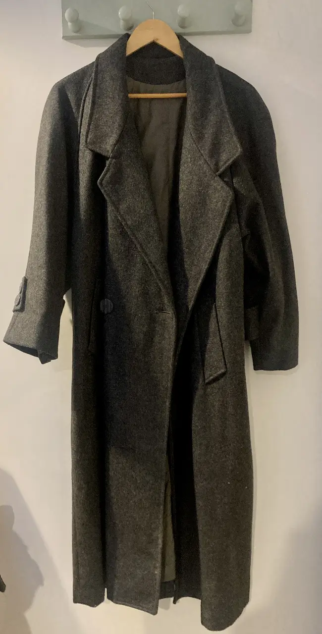 Sobretodo de paño gris oversized de sastrería, con corte clásico y solapas amplias. Tiene un diseño de pinzas en la unión del hombro con la manga, lo que genera un sutil efecto balloon. Está en impecable estado. El forro interno no tiene roturas y además posee los botones de repuesto cocidos adentro