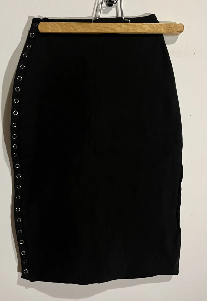 Pollera negra ajustable de ojalillos plateados a los costados. Un diseño moderno y canchero para lucir en cualquier salida.