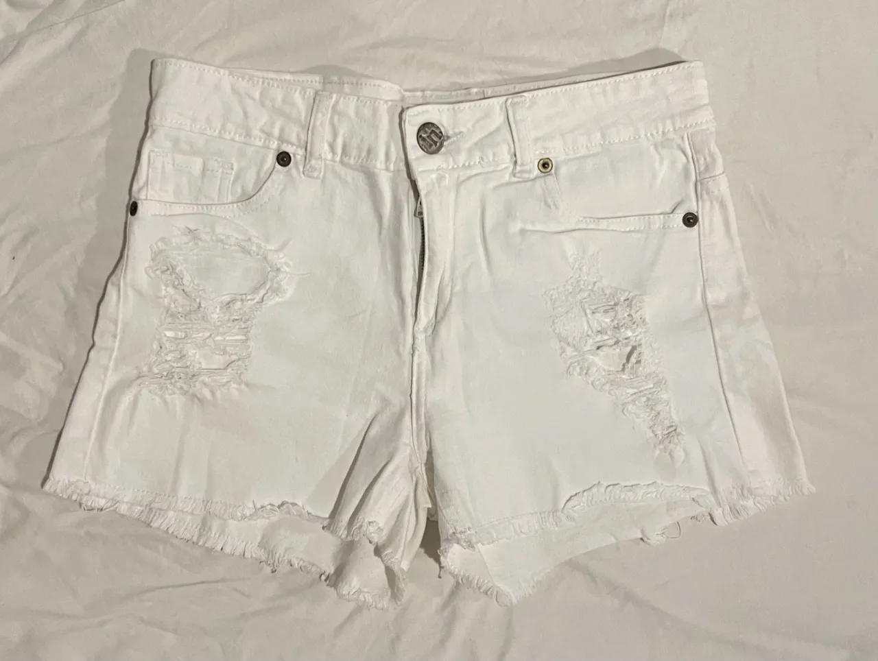 Shorts de jean blancos con roturas y detalles deshilachados en los bordes. Un básico súper canchero para armar looks de verano.