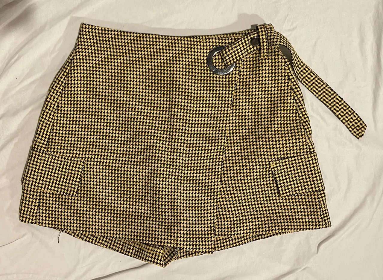 Shorts tiro alto con estampado pata de gallo en amarillo y negro. Tienen falsos bolsillos y un cinturón con hebilla metálica. Ideales para un look canchero y moderno.