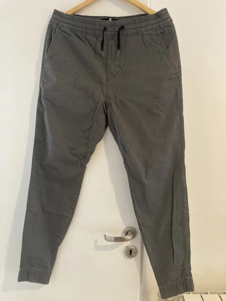 Pantalón jogger skinny de hombre, color verde. Confeccionado en tela de algodón con cintura elastizada y cordón ajustable. Bolsillos laterales y traseros. Ideal para un look casual y cómodo. HOLLISTER