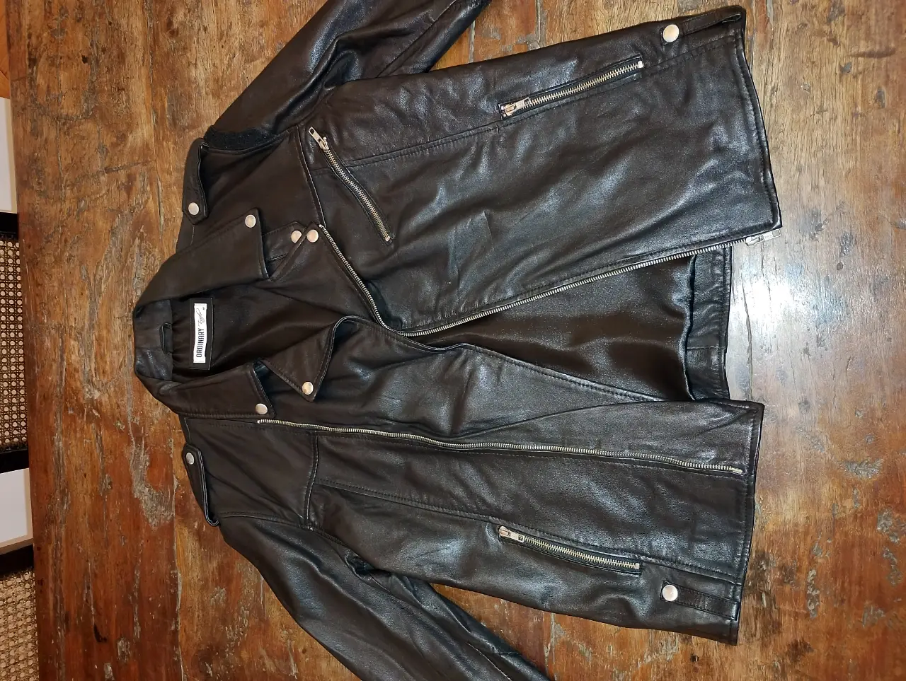 Chaqueta de cuero negra estilo biker, ideal para un look rocker o casual. Confeccionada en cuero sintético de alta calidad, presenta cierre y detalles metálicos. Cierres YKK. Botones metálicos algo gastados por el tiempo. La campera no tiene uso, el estado del eco cuero es excelente. 