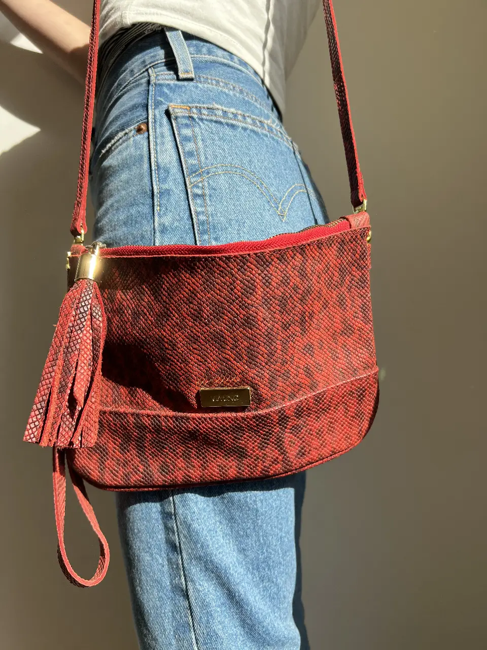 Bandolera roja con estampado de reptil. Detalles dorados y borla. Ideal para un look moderno y con estilo.